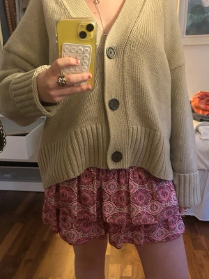 Rosa mönstrad kortkjol  - Supersöt kortkjol från MeetxTiger i rosa o lila toner med ett unikt paisleymönster. Kjolen har smock i midjan och volangig nederdel som ger en flowy känsla. Perfekt för dig som vill ha en färgglad och lekfull stil. Sjorts finns också under volang delen. Storlek är M/L men till o med passar S.