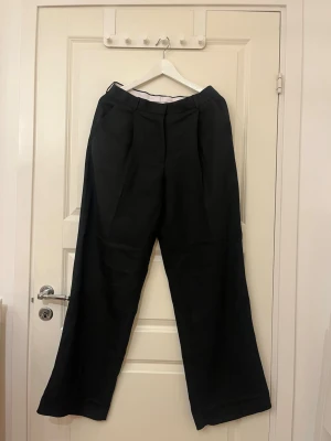 Svarta kostymbyxor från Dagmar - Snygga svarta kostymbyxor från Dagmar med hög midja och vida ben. Byxorna har inte varit använda. Värt att nämna är att dem som många andra kostymbyxor behöver sys upp till rätt längd vilket man ser på första bilden. 