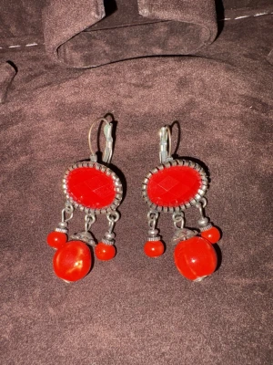 Röda vintage örhängen med pärlor - Unika örhängen med oval röd sten i silverfärgad infattning och tre hängande röda pärlor. Stenarna har en facettslipad yta och metallfästet har en retrovibe. Perfekt för dig som gillar färgstarka accessoarer och vill sticka ut.