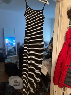 Svartvit långrandig klänning - Säljer en svart långklänning med vita ränder och tunna axelband. Klänningen har en smal passform och bär storlek M, men passar nog en S också! Helt ny som bara legat i garderoben som aldrig kommit till användning