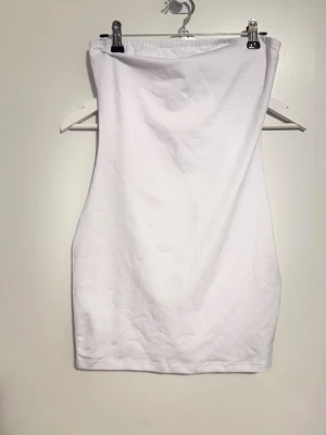 Kort vit bandå klänning - Säljer en enkel och stilren vit bandå klänning. Toppen är axelbandslös och har en rak, tight passform som sitter snyggt mot kroppen. Använd 1 gång 