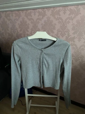 Grå ribbad kofta från Zara - Säljer en enkel och stilren grå kofta från Zara i storlek L men sitter som XS-S. Koftan är ribbad, har rund halsringning, långa ärmar och knäppning framtill. Perfekt att slänga över en topp eller bära som den är.
