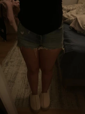 Blå jeansshorts med fransig kant - Säljer ett par klassiska blå jeansshorts med fransig kant och slitna detaljer. Shortsen har normal passform, fem fickor och dragkedja framtill. Perfekta till sommaren och ger en avslappnad vibe.