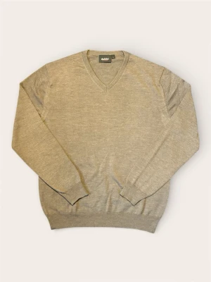 Beige stickad tröja från Dahlin - Snygg beige stickad tröja från Dahlin med v-ringad hals och diskret broderad logga på bröstet. Tröjan har långärmade ribbade muddar och är gjord i mjukt material som passar perfekt till lager-på-lager. Enkel och stilren design.