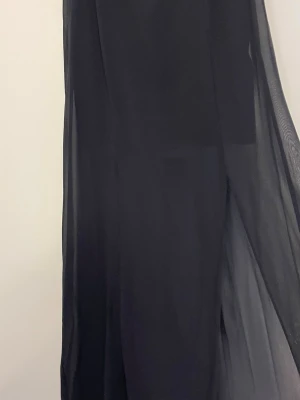 Svart långkjol i transparent tyg - Säljer en svart långkjol med ett snyggt transparent lager som ger en cool och luftig känsla. Kjolen har rak passform och är enkel att matcha med olika toppar. Perfekt för dig som gillar stilrena och minimalistiska plagg.