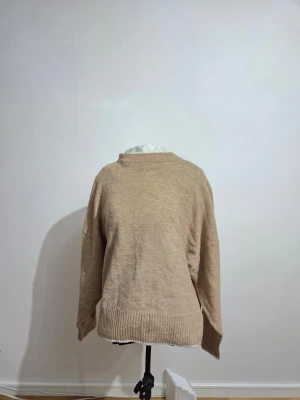 Beige stickad tröja från H&M - Mysig beige stickad tröja från H&M i storlek L. Tröjan har en rund halsringning, ribbade muddar vid ärmslut och nederkant samt långärmad passform. Perfekt för lager-på-lager under kyliga dagar.