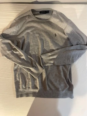 Grå Ralph lauren tröja - Slim fit grå tröja från Polo Ralph Lauren i mjuk pima bomull. Klassisk rund hals och långärmad design med diskret broderad logga på bröstet. Perfekt för dig som gillar stilrena och enkla plagg med snygg passform.