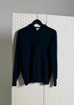 Mörkblå hoodie i kashmir från Soft Goat - Snygg mörkblå hoodie från Soft Goat i 100% kashmir. Tröjan har huva med snörning och långa ärmar, perfekt för dig som gillar mjuka och lyxiga material. Passformen är normal och den har en stilren look utan mönster eller extra detaljer.