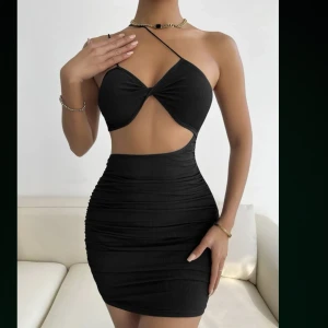 Svart cut out klänning från SHEIN - Svart kort klänning från SHEIN med smala axelband och trendig cut out-detalj framtill. Klänningen har tight passform, rynkade sidor och ribbad struktur. Perfekt för dig som vill sticka ut med en snygg och modern look. Klänningen är stretchig. Storlek L. Nypris 119kr