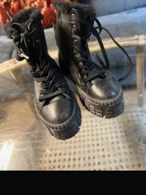 Svarta boots från Tamaris med fuskpäls - Säljer ett par chunky svarta boots från Tamaris i storlek 37. Skorna har grov sula, snörning, dragkedja på sidan och är fodrade med mjuk fuskpäls. Tillverkade i skinnimitation och perfekta för kalla dagar.