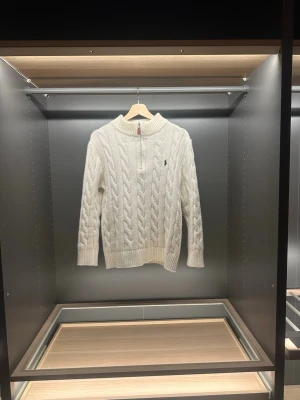 Polo Ralph Lauren quarter zip - Säljer en vit kabelstickad tröja från Polo Ralph Lauren med half zip och ribbad krage. Tröjan har lång ärm och klassisk broderad logga på bröstet. Perfekt för kyliga dagar och har en snygg, tidlös look.