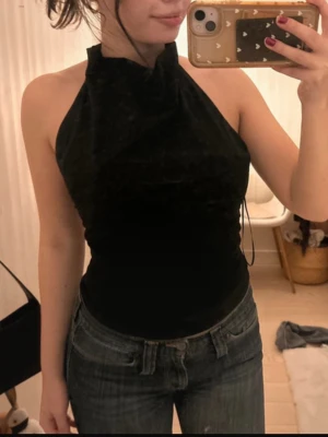 Svart  halterneck topp - Säljer en svart halterneck topp . Toppen är ärmlös och har en hög hals som ger en snygg och stilren look. Perfekt att matcha med jeans eller kjol för en cool vibe.