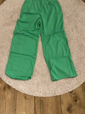 Gröna wide byxor från Monki - Säljer ett par gröna byxor från Monki i storlek 38. Byxorna har en rak och vid passform med hög midja och bälteshällor. Tillverkade i ett mjukt bomullsliknande material som känns skönt mot huden. Perfekta för dig som vill ha en färgklick i garderoben!
