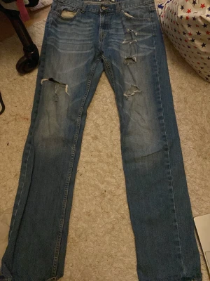 Blå slitna jeans med raka ben - Dör för de!! Men hade de under min drainer period när jag alltid gick runt med Yung lean i hörlurarna och rockade de här byxorna, nu är perioden tyvörr över och jag vill helst inte se de är något mer, men vill veta att de ligger i säkra händer så…Säljer ett par blå jeans med raka ben och flera slitningar och hål på framsidan. Klassisk femficksmodell med broderad bakficka. Jeansen har en cool, avslappnad vibe och är gjorda i robust denim. JAG ÄR TJEJ OCH HAR HAFT PÅ MIG DE STRUNTA I DRESSMAN!