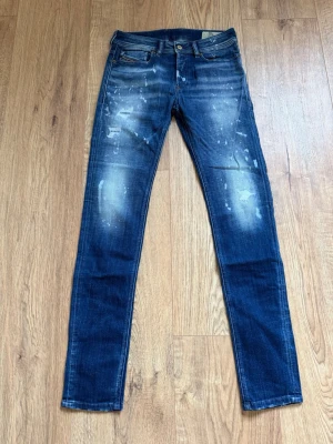 Blå skinny jeans från Diesel, stl 28 / 32 HELT NYA - Säljer ett par blå skinny jeans från Diesel med coolt blekt och prickigt mönster. Jeansen har klassisk femficksdesign, knapp och dragkedja fram samt Diesel-logga bak. Materialet är 94% bomull, 4% polyester och 2% elastan för skön stretch.