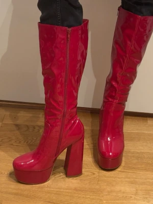 Glossy röda högklackade stövlar  - Röda stövlar med hög klack och tjock sula som använts en gång. Minns tyvärr ej vart jag köpte dem.