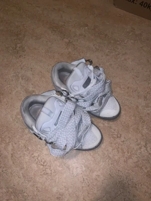 Lanvin curbs  - Säljer ett par chunky vita Lanvin sneakers med breda, mönstrade snören och grå sula. Skorna har detaljer i skinn och mocka, samt metallöglor för snörningen. Kommer i originalkartong och dustbag. Perfekt för dig som gillar statement sneakers.