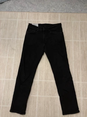 Svarta regular fit jeans från H&M - Svarta jeans från H&M med regular fit och klassisk femficksdesign. Jeansen har rak passform och är tillverkade i ett mjukt bomullsmaterial med lite stretch för extra komfort. Jeansen har blivit använda ett par gånger och är i ett bra skick. Killen i bilden är 172 cm för referens.