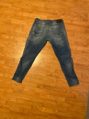 Replay Denim blå jeans tapered fit - Blå jeans från Replay Denim med snygga slitningar och klassisk femficksdesign. Tapered fit med normal passning och detaljerad brodering på bakfickorna. Märkespatch i svart skinn vid midjan. Perfekta för dig som gillar stilrena jeans med lite edge.