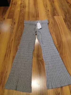 Grå kabelstickade byxor M - Mysiga grå kabelstickade byxor i storlek M med bred resår i midjan och snörning. Byxorna har ett loose fit och är tillverkade i mjukt stickat material. Perfekta för chill dagar hemma eller när du vill vara extra bekväm. Nypris 359 kr