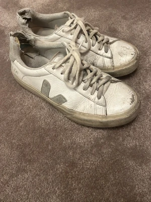 Vita Veja sneakers med grå detaljer - Säljer ett par klassiska Veja sneakers i vitt skinn. Har änvänts mycket och har många tecken på slithet.