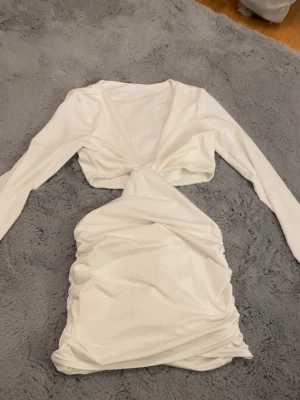 Vit omlott kortklänning med lång ärm - Säljer en vit kortklänning med lång ärm och snygg omlott-detalj framtill. Klänningen har rynkade partier på kjolen och en cool twistad midja som ger en unik look. Perfekt för dig som gillar trendiga och stilrena plagg med lite edge. Kan eventuellt tänka mig gå ner i pris