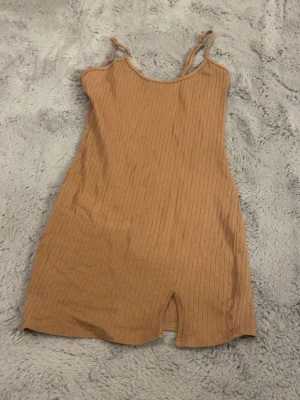 Ribbad beige kortklänning - Säljer en ribbad beige kortklänning med smala axelband och en liten slits framtill. Klänningen har en enkel och stilren design som är lätt att matcha. Perfekt för varma dagar och enkel att styla med accessoarer. Kan eventuellt tänka mig gå ner i pris