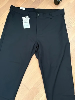 Svarta / mörkblåa kostymbyxor från Zara - Snygga svarta kostymbyxor från Zara med klassisk rak passform och midwaist. Byxorna har bälteshällor, knappstängning fram och två bakfickor med knapp. Perfekta för en stilren look och tillverkade i ett mjukt material som ger bra komfort.