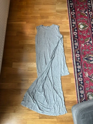 Grå långklänning Acne Studios - Säljer en stilren grå långklänning från Acne Studios. Klänningen är ärmlös och har en rak, enkel siluett i mjukt bomullsmaterial. Perfekt för dig som gillar minimalistisk design och vill ha något bekvämt och snyggt.