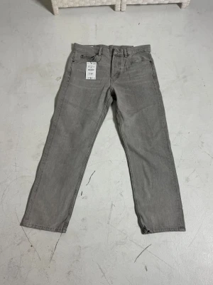 Grå Zara jeans  - Helt oanvända jeansbyxor från Zara i rak modell med klassisk femficksdesign och bälteshällor. Byxorna har en neutral grå färg och är tillverkade i slitstarkt bomullsmaterial. Passar dig som gillar enkel och stilren look. Storlek 42 (Zara mått).