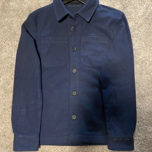 Donce de la sensé overshirt - Oanvänd mörkblå overshirt från Donce de la sense med klassisk krage, två bröstfickor och knäppning framtill. Den är i mjukt material och passar perfekt till lite kyligare dagar. Overshirten sitter perfekt på mig som är 178! (Se bild 4)