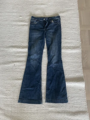 Blå flared jeans från H&M - Säljer ett par blå jeans från H&M med flared ben och midwaist. Jeansen har klassisk femficksdesign, justerbar midja och snygga slitningar. Perfekt för dig som gillar retrovibbar och vill ha ett statement-plagg i garderoben.