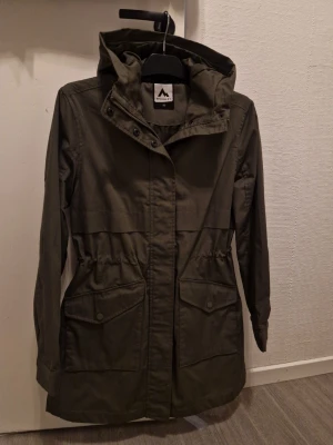 Grön parkajacka från McKinley - Säljer en snygg grön parkajacka från McKinley med huva och stora fickor framtill. Jackan har dragsko i midjan för bättre passform och stängs med både dragkedja och knappar. Perfekt för dig som gillar outdoor och vill ha en stilren look. Helt ny utan prislapp, nypris 799:- 