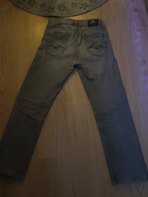 Replay grå jeans, rak modell - Säljer ett par grå jeans från Replay i rak modell med klassiska fem fickor och snygga detaljer på bakfickorna. Jeansen har normal passform och är tillverkade i slitstarkt bomullsmaterial. Perfekt för dig som gillar stilrena och tidlösa jeans.