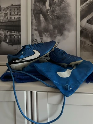 Nike Tiempo blå fotbollsskor - Säljer ett par Nike Tiempo fotbollsskor i blått med vita och svarta detaljer. Skorna har snörning och en platt sula med dobbar för gräsplan. Materialet är syntet och skinn, och de har en rund tå. Perfekta för dig som vill ha snygga och funktionella skor på planen. Är i väldigt bra skick då jag bara andvädit dom i några veckor.