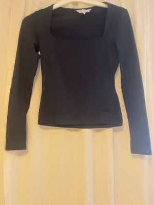 Svart långärmad topp med fyrkantig ringning - En stilren svart topp med lång ärm och fyrkantig ringning. Toppen har en slim passform och är tillverkad i ett mjukt stretchigt material, perfekt att matcha med jeans eller kjol. Enkel och clean design utan synliga detaljer.
