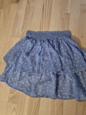 Blå volangkjol med små vita  blommor - Blå kortkjol med volanger och små vita blommor. Jätte skön och fin att ha på sig. 