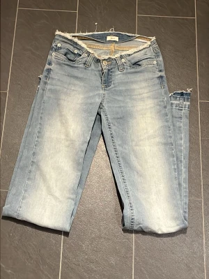 Ljusblå jeans med rå kant från Nelly - Säljer ett par ljusblå jeans från Nelly med rå, fransig kant upptill. Jeansen har klassisk femficksdesign, knapp och dragkedja fram samt en tvättad look med slitningar. Perfekt för dig som gillar en avslappnad och trendig stil.