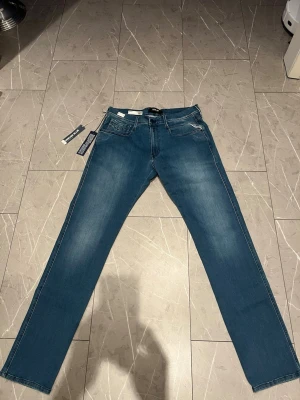 Replay Hyperflex Anbass jeans blå - Blå Replay Hyperflex Anbass jeans med slim fit och klassisk femficksdesign. Jeansen är handgjorda och färdigställda i Italien, tillverkade av återvunnen bomull och polyester för extra stretch och hållbarhet. Snygga detaljer och diskret tvättad look. Byxorna är helt nya, inte ens provade. Tveka inte att skriva för frågor eller annat
