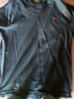 Svart t-shirt från Polo Ralph Lauren - Svart t-shirt från Polo Ralph Lauren i storlek XL. Klassisk design med korta ärmar och rund hals. Materialet är mjuk bomull och på bröstet finns den ikoniska röda Polo-loggan broderad. Perfekt för en chill och stilren look.