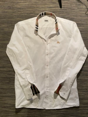 Vit Burberry skjorta med rutig krage - Säljer en riktigt snygg vit burberry skjorta! Skjortan är i mycket bra skick och har inga defekter. Fraktar samma dag som köp! Den kanske ser lite gul ut på bilden men det är studielampan i bakgrunden som reflekterar😅 Om ni har några frågor så är de bara att höra av er😊