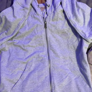 Grå hoodie från Burberry med dragkedja - Snygg grå hoodie från Burberry med klassiskt rutigt foder i huvan. Tröjan har hel dragkedja, snörning i huvan och två fickor framtill. Perfekt för dig som vill ha en stilren och exklusiv look med ikoniska Burberry-detaljer. Helt oanvänd burberry hoodie, priset kan också diskuteras 