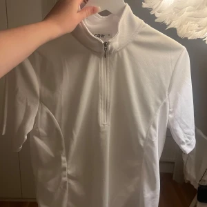 Vit tävlings topp - Säljer denna tävlings toppen från CRW, köpt på Hööks. Säljer pågrund av att den inte kommer till användning. Endast använd 1 gång och har inga defekter eller liknande. Den är normal i storleken.  Hör gärna av er vid frågor eller funderingar! 💞