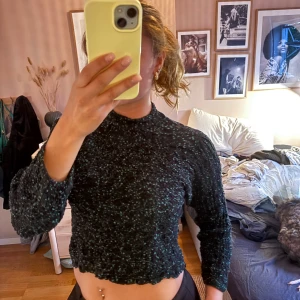 Svart-grön croppad tröja från Zara - Croppad svart tröja från Zara med gröna detaljer och lätt struktur. Tröjan har lång ärm, hög hals och vågig kant nertill. Perfekt för dig som gillar en trendig och bekväm look med lite extra edge.