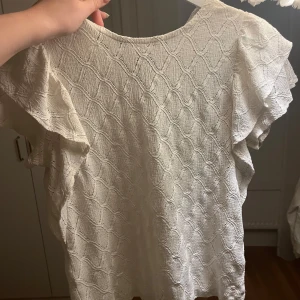 Vit blus från Holly & Whyte - Supersöt vit blus från Holly & Whyte med strukturmönster och volangiga korta ärmar. Blusen har en lätt och luftig känsla, perfekt till varmare dagar. Tillverkad i ett mjukt tyg som känns skönt mot huden. Nästan aldrig använd och normal i storleken. Hör gärna av er vid frågor eller funderingar! 💕