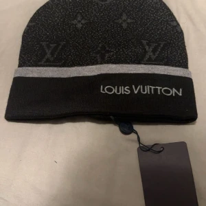 Svart mössa  - Snygg svart mössa från luis Vuitton med diskret mönster och logotyp. Perfekt för att hålla stilen i kallare väder 