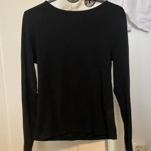 Svart långärmad basic tröja - En enkel svart långärmad tröja med rund hals. Perfekt för lager-på-lager och passar till allt. Mjuk och skön, troligtvis i bomull eller polyester. Stilren och clean look som funkar till jeans eller kjol.