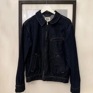 Mörkblå jeansjacka från BDG - Säljer en stilren mörkblå jeansjacka från BDG Urban Outfitters. Jackan har dragkedja framtill, klassisk krage och flera fickor med snygga kontrastsömmar. Perfekt för dig som gillar en enkel men trendig look.