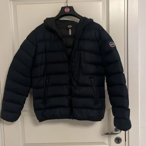 Mörkblå dunjacka från Colmar - Snygg mörkblå dunjacka från Colmar med huva och två dragkedjeförsedda fickor. Jackan har quiltad design och är perfekt för kalla dagar. Den är lätt och har en normal passform, vilket gör den enkel att bära till jeans eller hoodie. Ny pris runt 3500kr 
