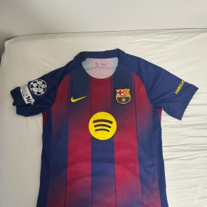 FC Barcelona Lamine Yamal matchtröja - Säljer en officiell FC Barcelona matchtröja från Nike med Lamine Yamal och nummer 10 på ryggen. Tröjan är kortärmad, har klassiska blå och röda ränder, gula detaljer och klubbmärke på bröstet. Materialet är lätt och andas, perfekt för fotboll eller samling. Home kit 2025/26